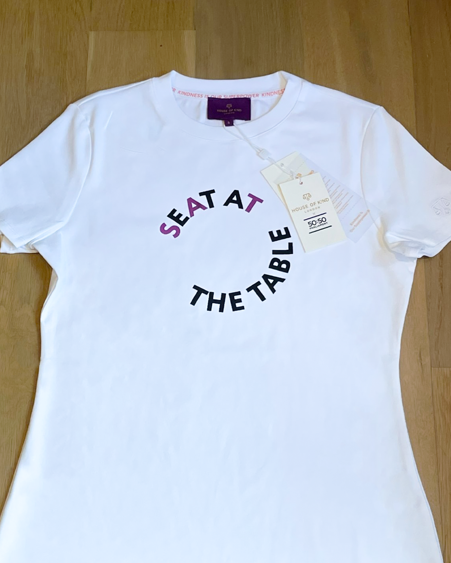 White t-shirt with 'SEAT AT THE TABLE' text on a wooden surface