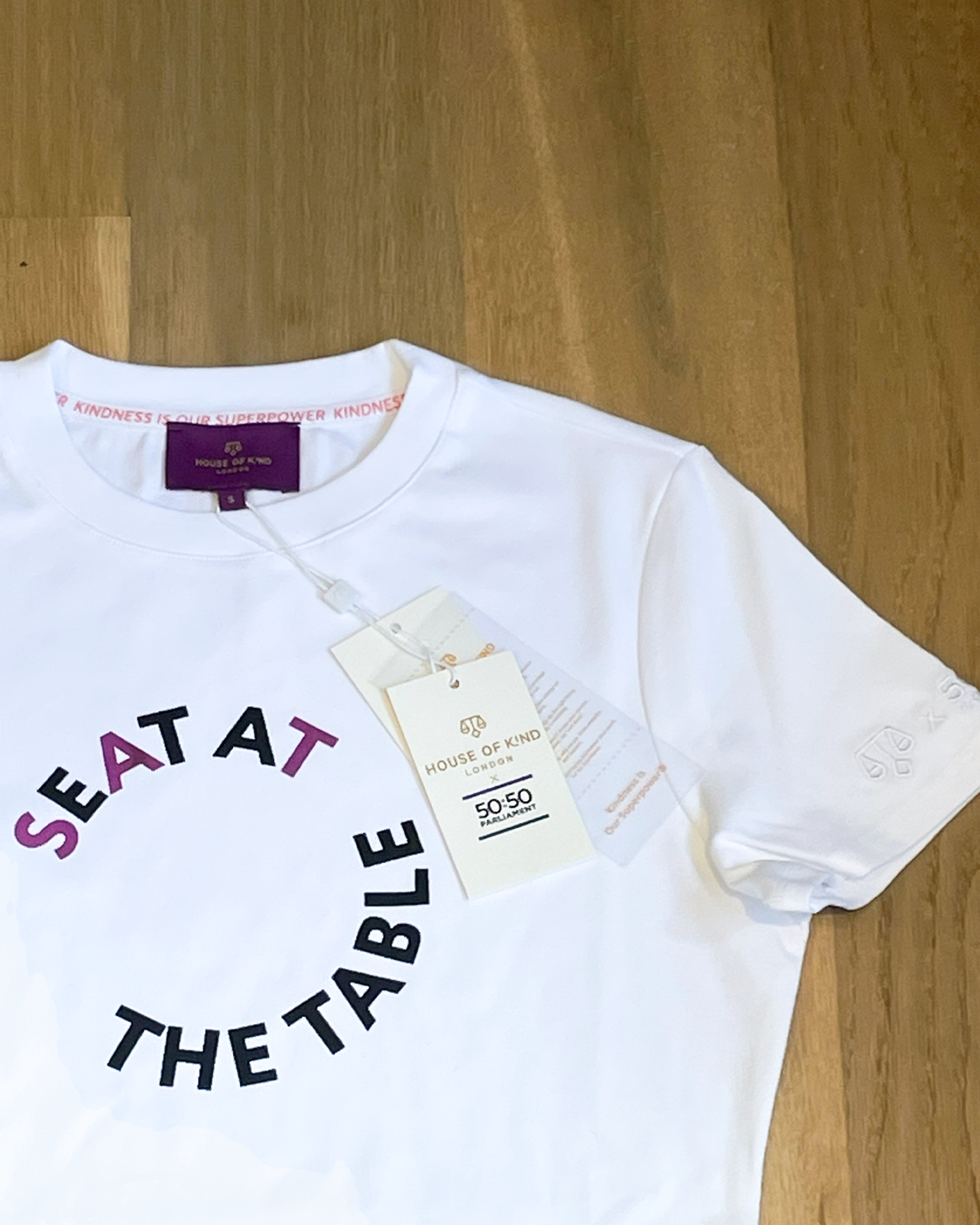 White t-shirt with 'Seat at the Table' text on a wooden floor