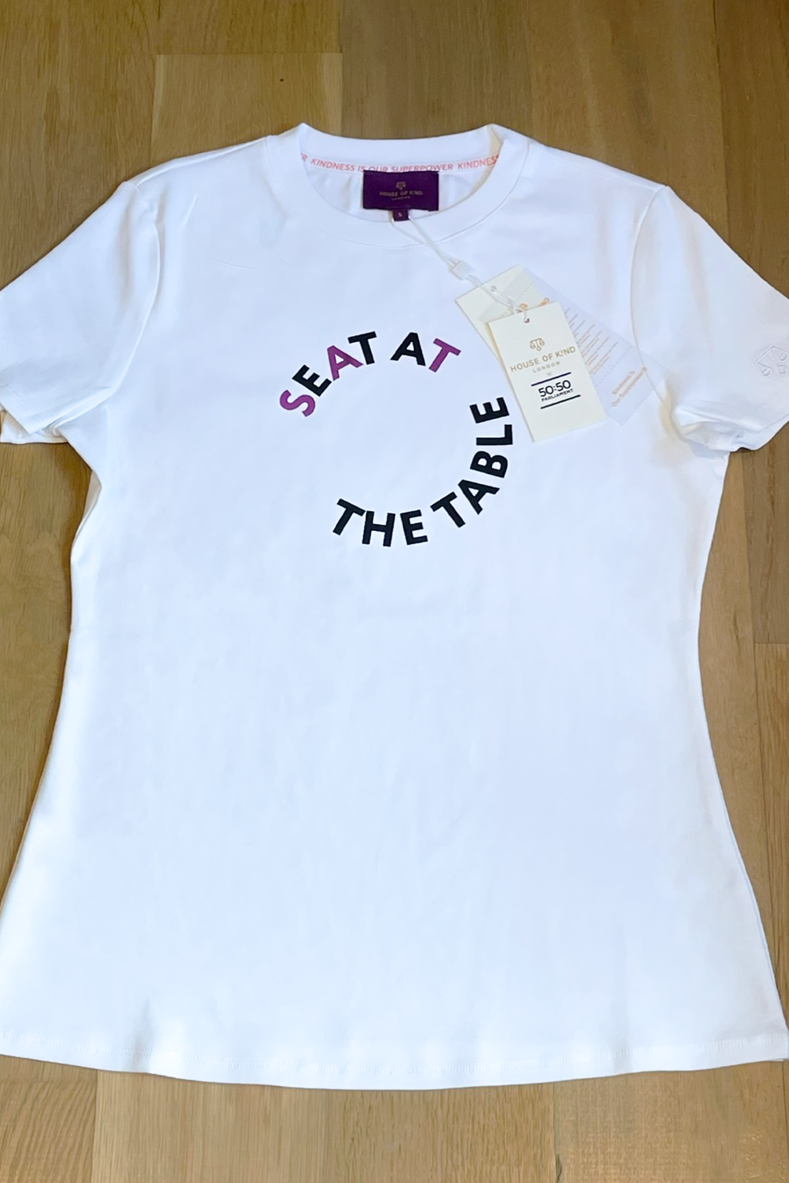White t-shirt with 'SEAT AT THE TABLE' text on a wooden surface