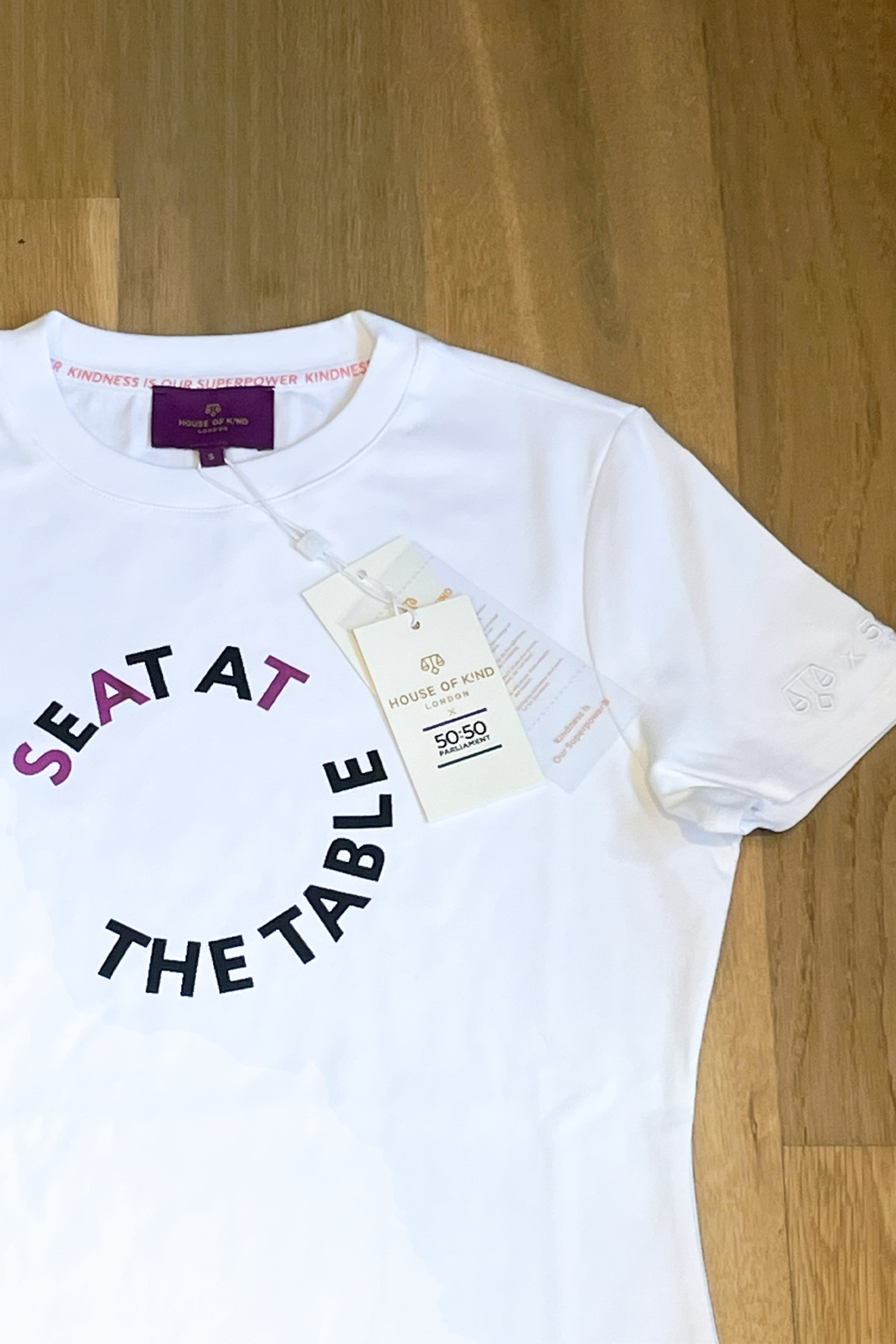 White t-shirt with 'Seat at the Table' text on a wooden floor