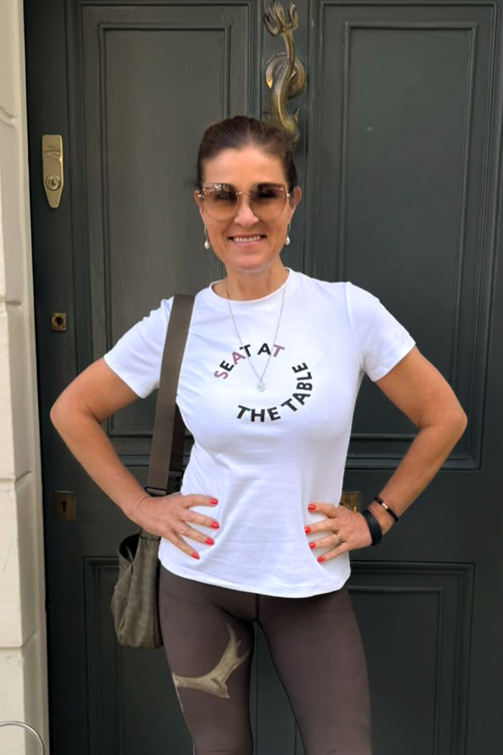 Woman wearing a white t-shirt with text standing in front of a door.